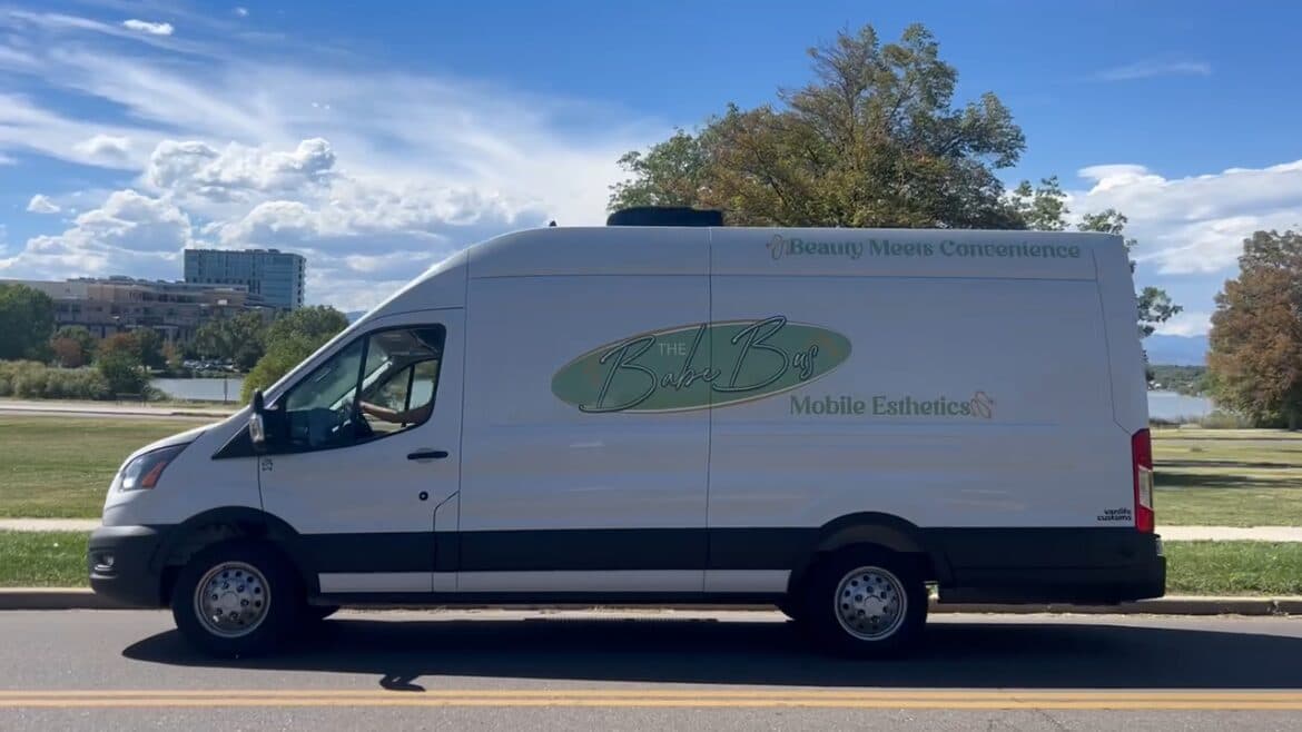 The Babe Bus van parked at the curb, with trees and a city skyline behind it